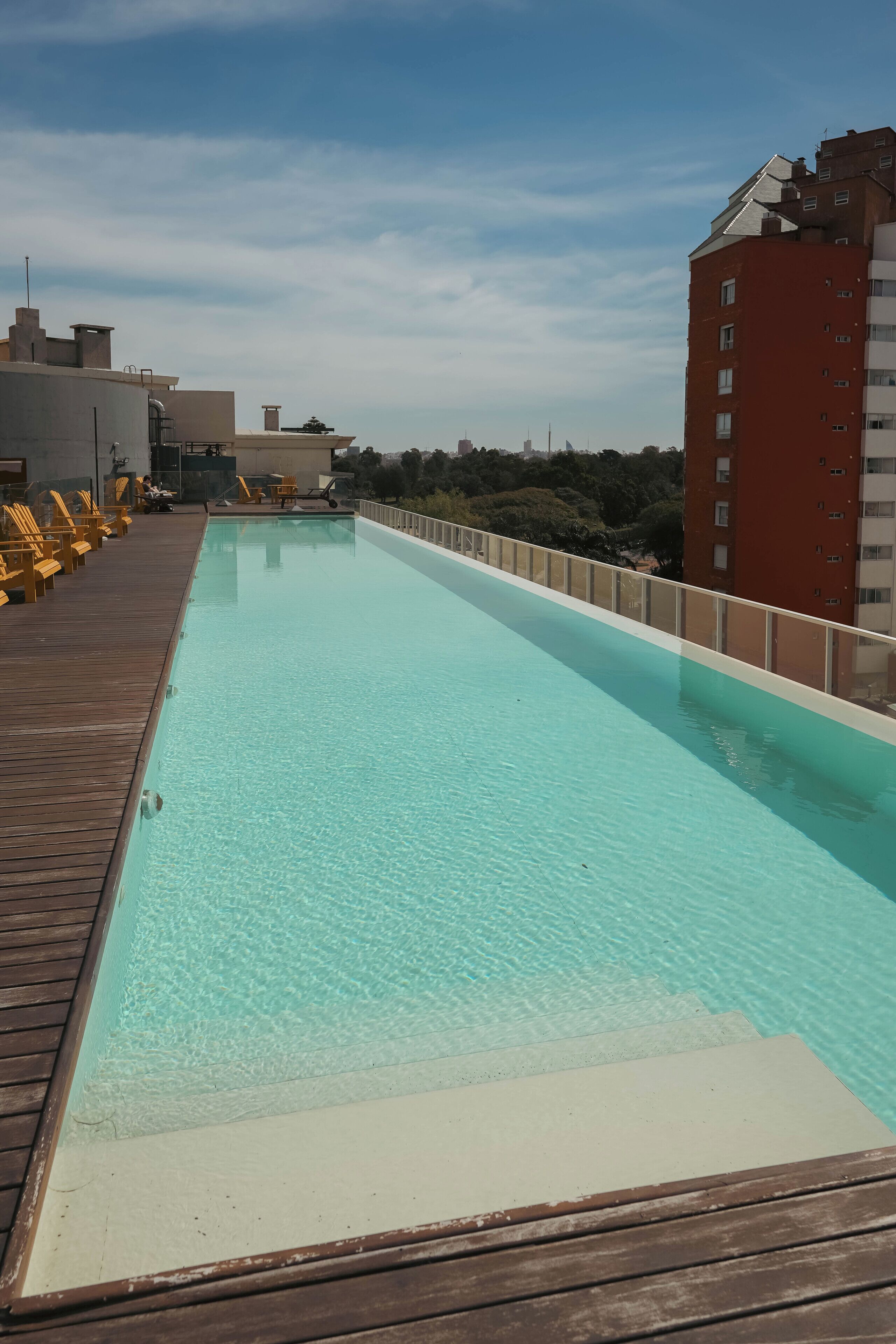 A rectangular swimming pool with a wooden deck and yellow chairs on one side.