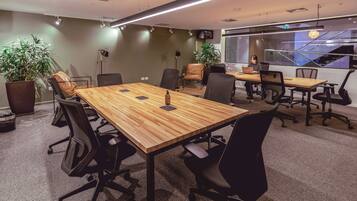Una sala de conferencias moderna con una mesa de madera, sillas de oficina negras y plantas en macetas.