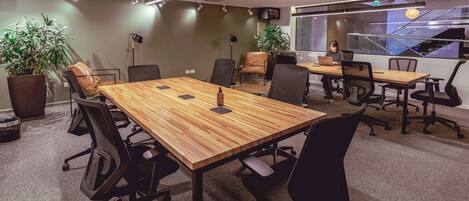 Una sala de conferencias moderna con una mesa de madera, sillas de oficina negras y plantas en macetas.