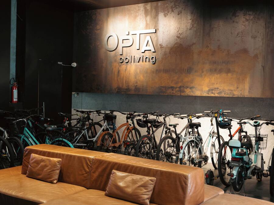 Un área de descanso moderna con un amplio sofá de cuero, un perchero para bicicletas en la pared, y un letrero que dice "OPT A cycling".
