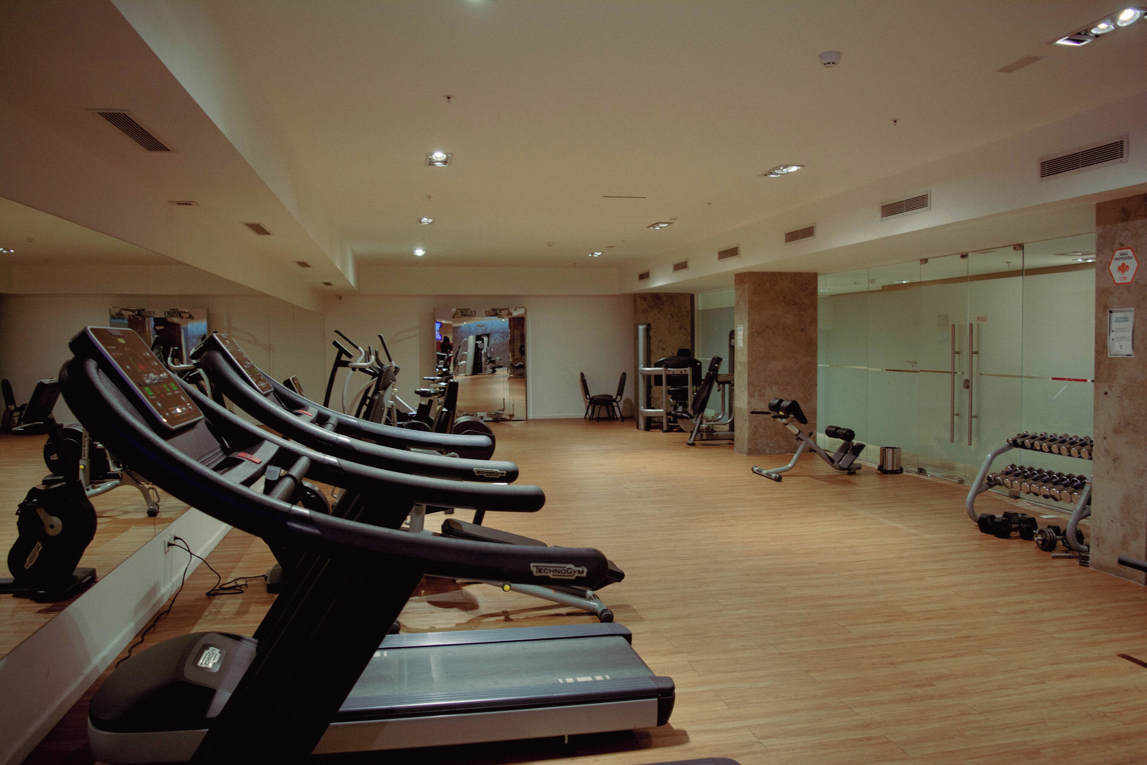 Un gimnasio con cintas de correr, bicicletas estáticas y pesas libres.