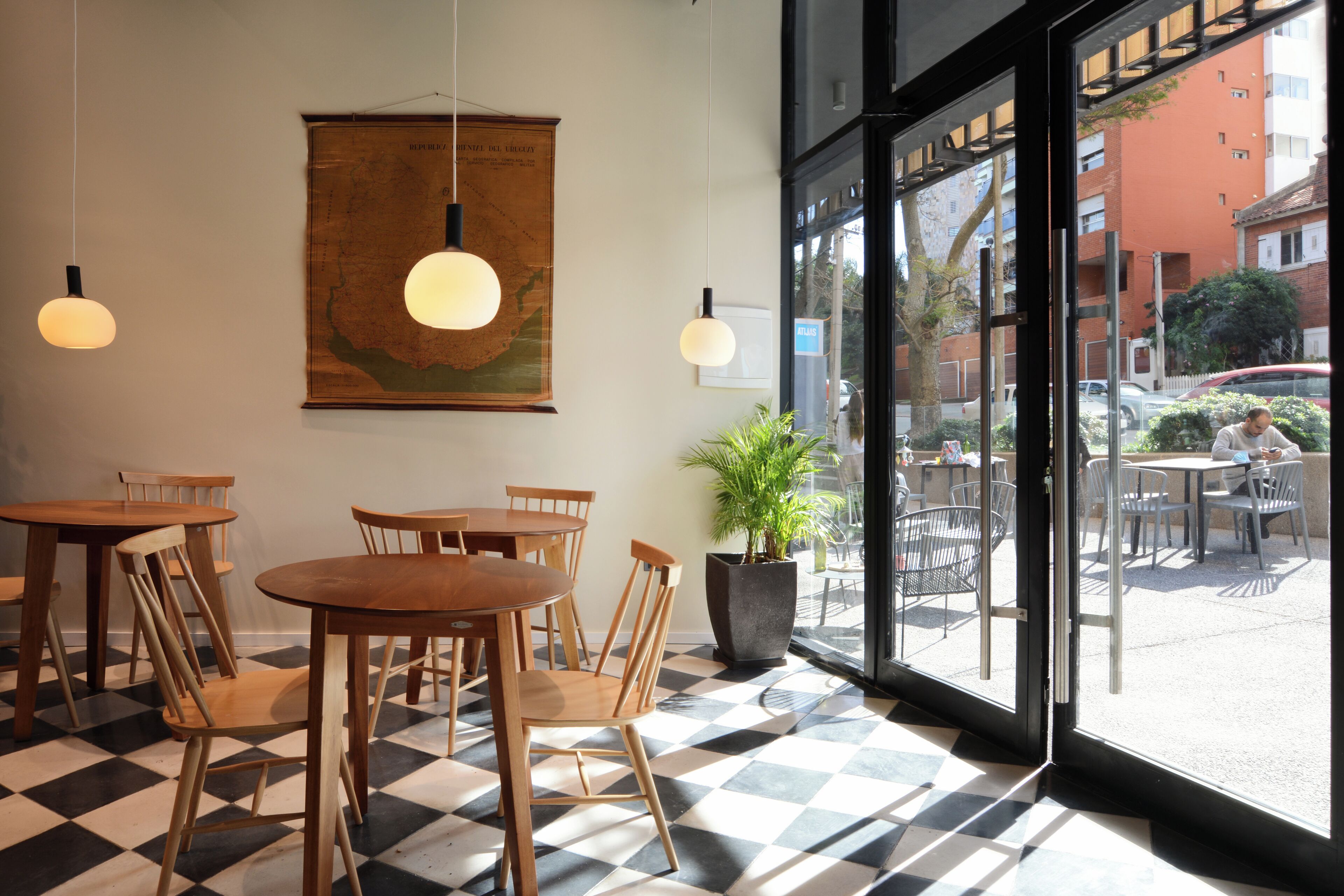 Ein Café-Interieur mit Holztischen und -stühlen, einer großen Karte an der Wand und Blick auf die Straße.