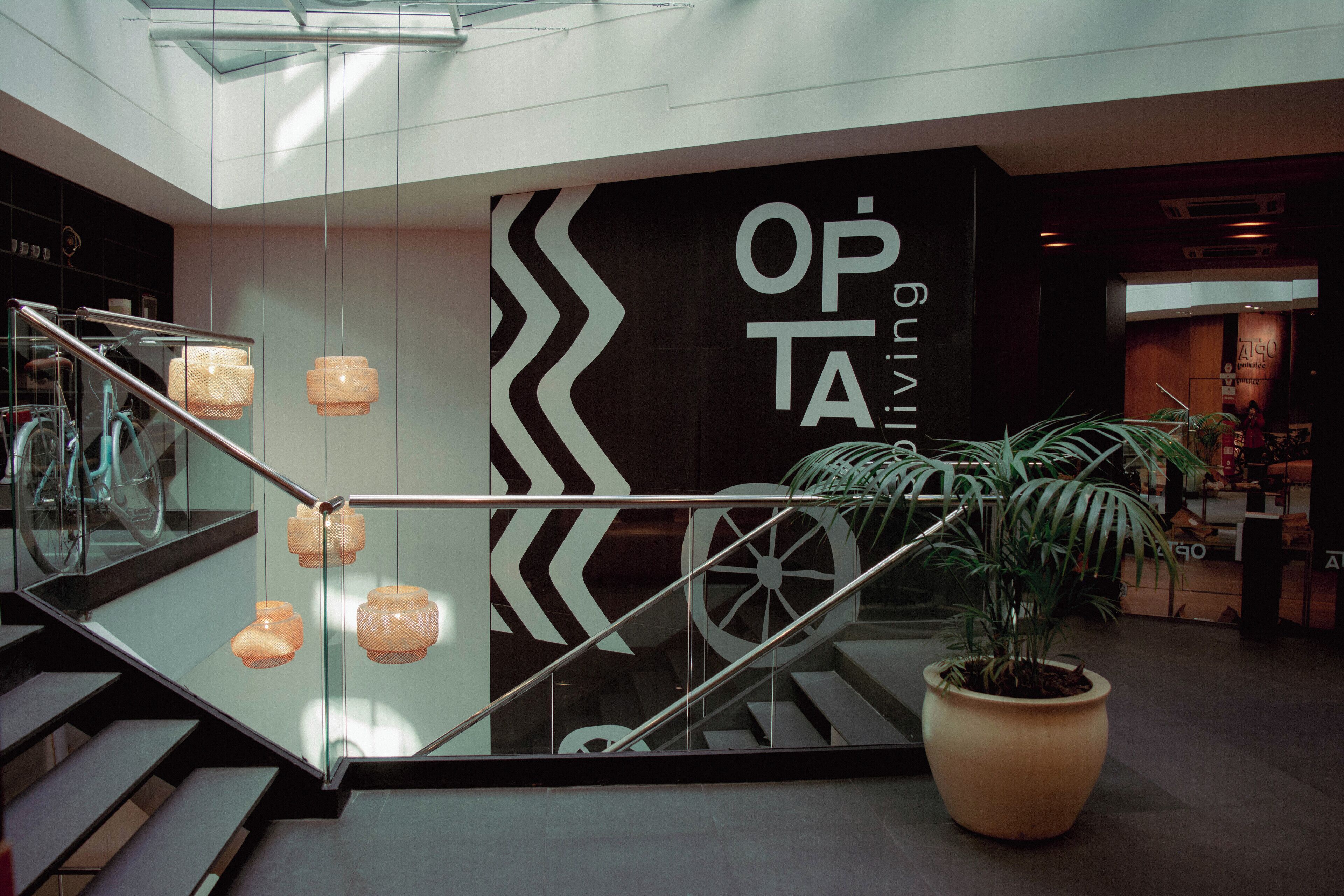 Un interior moderno con una escalera de cristal, una gran planta en maceta y una pared con el texto 'OPTIMISING'.