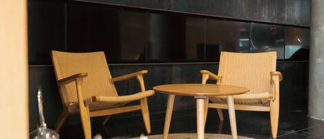 Un interior moderno con dos sillones de mimbre y una pequeña mesa, una escultura decorativa de metal y una pared oscura con una cámara de seguridad.