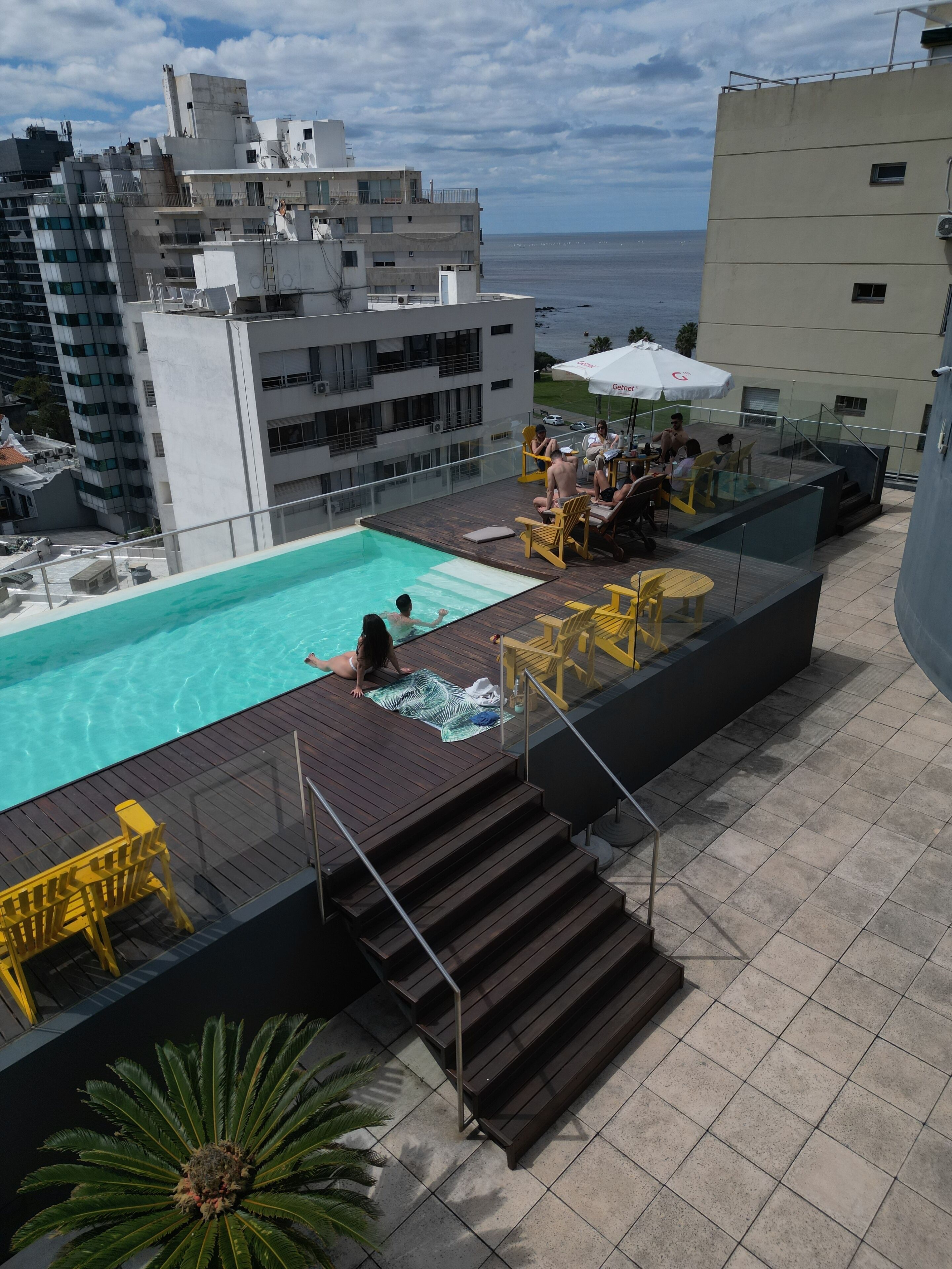 A rooftop pool area with a clear view of the sea, surrounded by modern buildings.