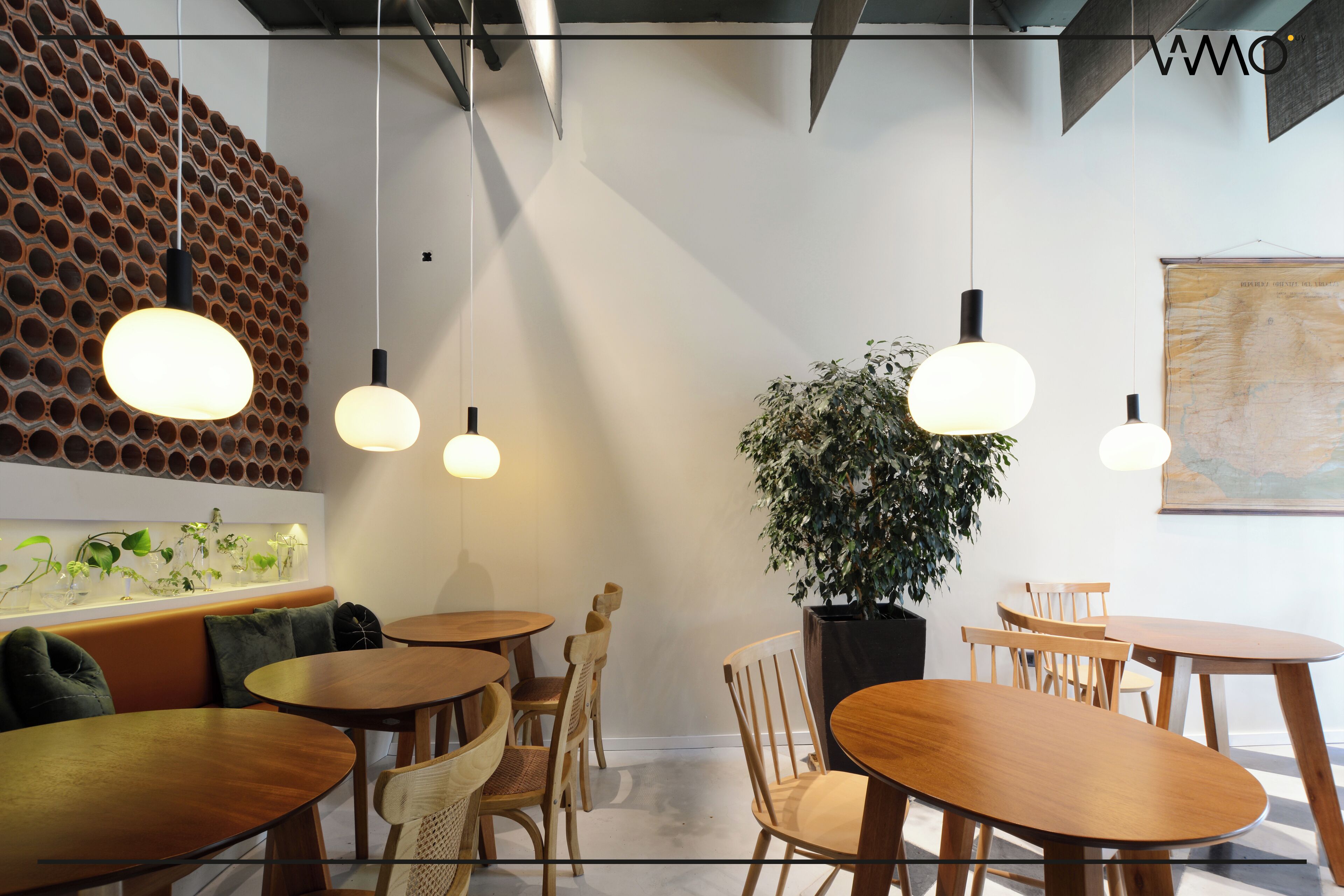 Un interior moderno con mesas y sillas de madera redondas, una planta grande en maceta y un muro original con diseños circulares.