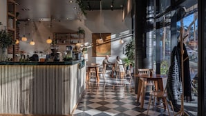 A cafe with a checkered floor, wooden furniture, hanging plants, and a counter with various items. - Opta Coliving (Montevideo)