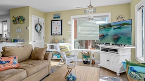A living room with a beige couch, white wicker chair, a television, and a wicker basket.