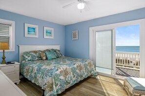 A bedroom with a bed, a nightstand, a lamp, and a view of the ocean through a sliding glass door.