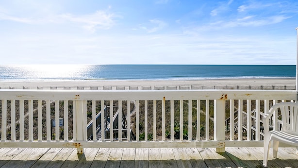 A wooden deck with a white railing overlooking a beach.