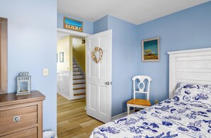 Un dormitorio con una cama, un aparador, una silla, un cuadro y una escalera que lleva a otra habitación.