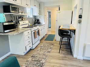 Una cocina con gabinetes blancos, microondas, estufa y refrigerador.