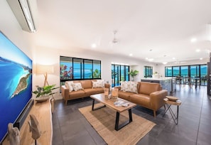 A spacious living area with a large window, a sofa set, a coffee table, and a kitchen area in the background.