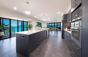 A modern kitchen with a large island, dark cabinetry, and a view of the sea. - Airlie Oasis (Airlie)