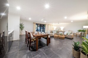 A modern living room with a dining area, a sofa set, and a kitchen visible in the background. - Airlie Oasis (Airlie)