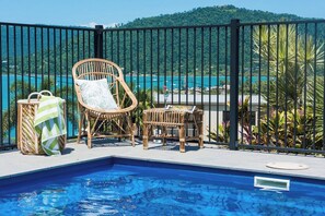 Ein Poolbereich mit Blick auf ein Gewässer und Hügel, umgeben von einem schwarzen Metallzaun.