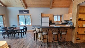 Une cuisine avec des meubles en bois, un plan de travail noir et un coin bar avec des tabourets. Deux fenêtres laissent entrer la lumière naturelle.