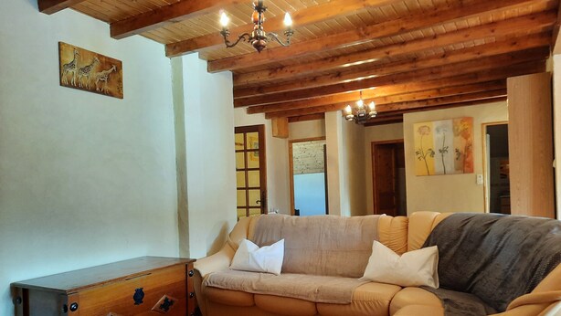 Uma sala de estar acolhedora com teto de madeira, um sofá bege, um baú de madeira e um candelabro.