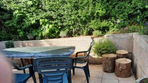 Um pátio externo com mesa e cadeiras, cercado por vegetação e uma parede de pedra.