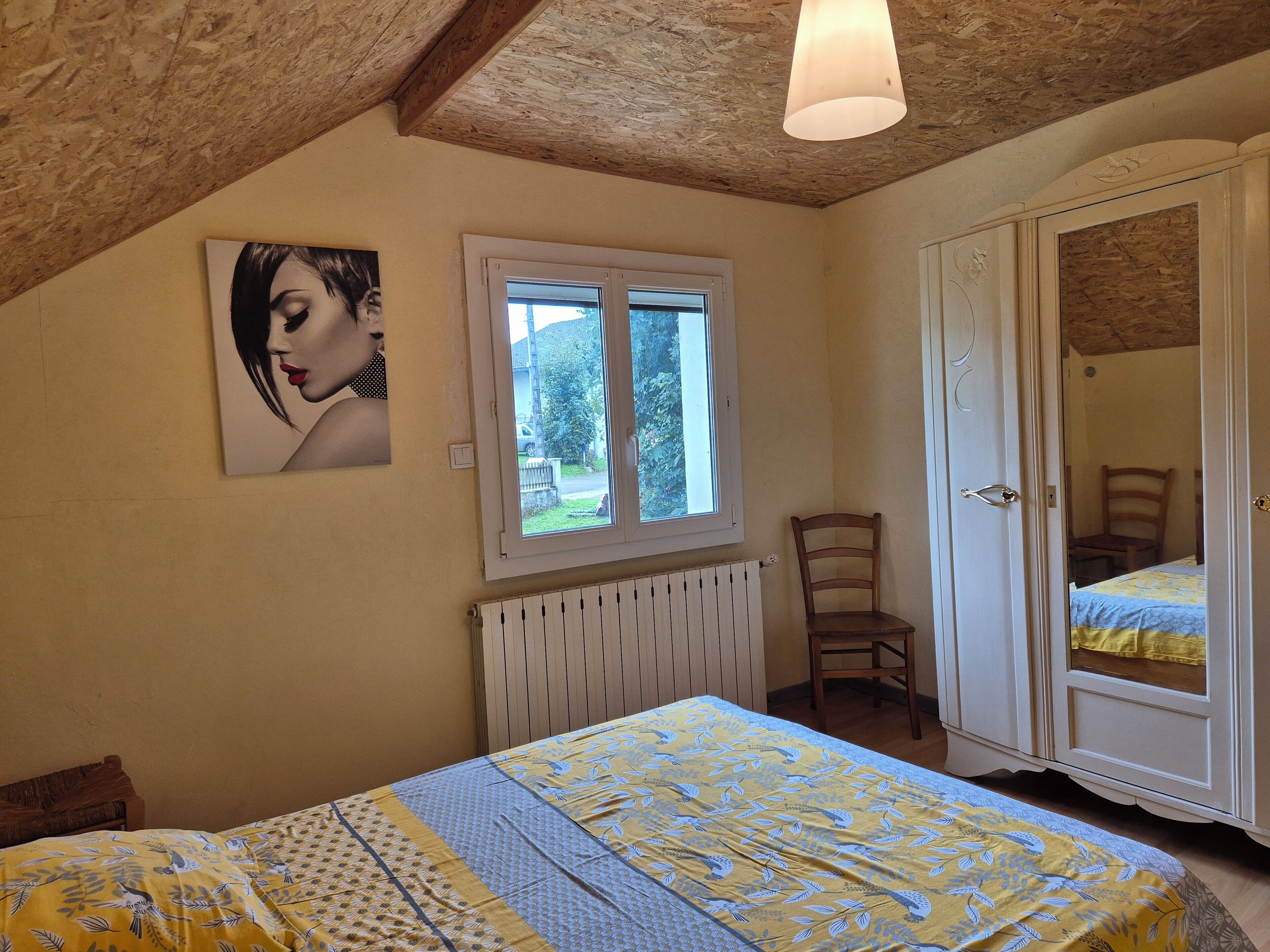A bedroom with a bed, a radiator, a window, a chair, and a wardrobe.