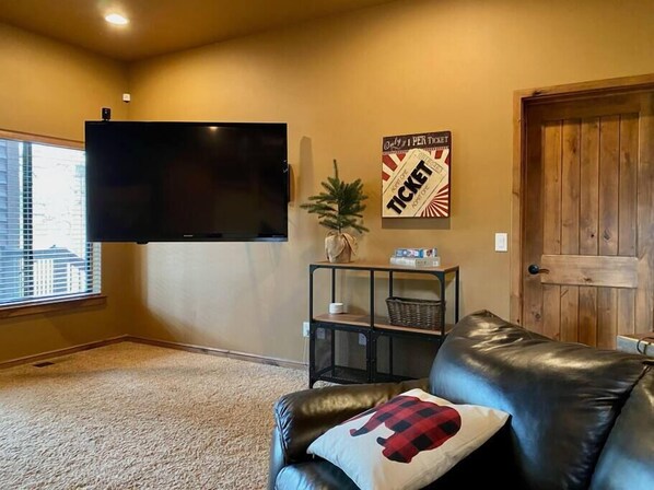 Een woonkamer met een zwarte leren bank, een flatscreen televisie aan de muur, een houten deur en een raam met zonwering.