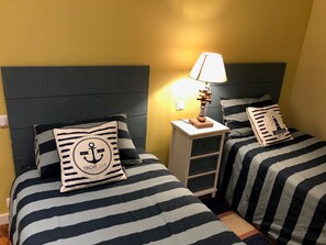 Ein Zimmer mit zwei Betten, jeweils mit gestreifter Bettwäsche und passenden Kissen, einem Nachttisch mit Lampe und einer Wandleuchte.