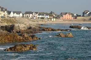 En kystby med huse langs stranden og klippeformationer i vandet.