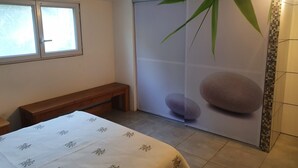 A room with a bed, a bench, a sliding door with a bamboo and stone design, and a window. - 50 m2 basement apartment (ceiling height 1.80 m) (Figari)