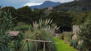 A lush garden with a swing set, a stone wall, and a view of a mountain range. - 50 m2 basement apartment (ceiling height 1.80 m) (Figari)