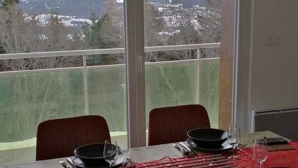 A dining table set for four with a mountain view through large windows. - Apartment Font Romeu (Font-Romeu-Odeillo-Via)