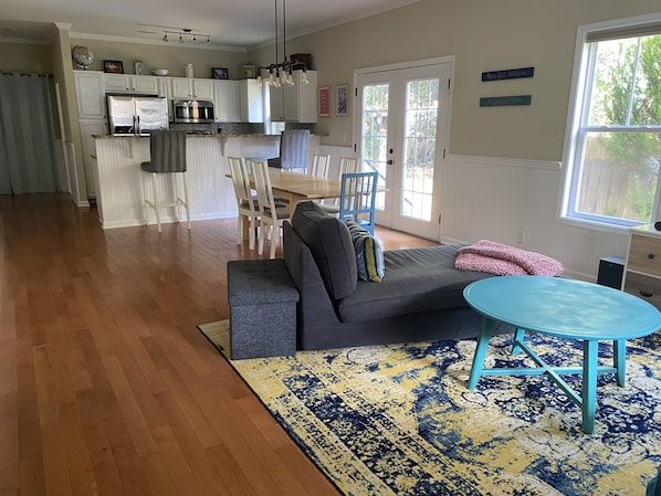 A spacious living room with a grey sofa, a blue table, and a patterned rug.