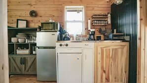 A compact kitchen with a refrigerator, microwave, and sink. There are wooden cabinets and a window above the sink.