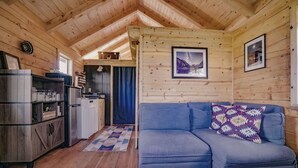 A cozy cabin interior with a blue sofa, wooden walls, a kitchen area, and a dining table.