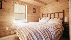 A wooden cabin bedroom with a bed, a window, and a nightstand.