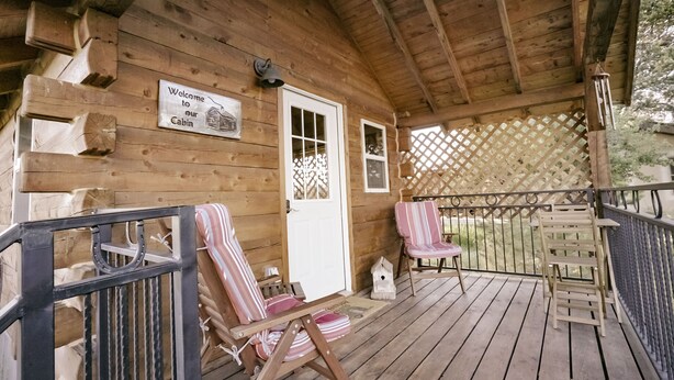 A wooden cabin with a porch, a welcome sign, and two striped chairs.
