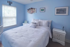Un dormitorio con una cama grande, una mesita de noche con cajones, una ventana con persianas y decoración de pared que incluye un cuadro enmarco y un collage con temática de automóviles.