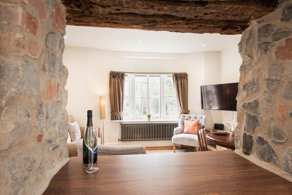 A cozy room with stone walls, a wooden floor, a comfortable sofa, a dining table, and a television.