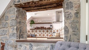 Un salon chaleureux avec un mur en pierre, un fauteuil gris agrémenté d’un coussin rouge et un plancher en bois.