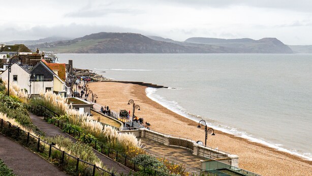 Une promenade en bord de mer, avec une plage, une digue et un sentier menant à un bâtiment doté d’un balcon.