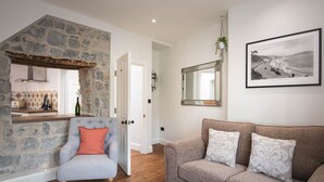 Un salon chaleureux avec un mur en pierre, un coin repas en bois, un fauteuil gris et un canapé marron.
