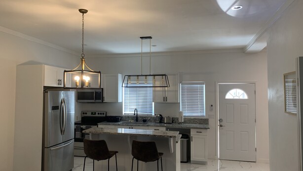 Cocina moderna con una isla central, electrodomésticos de acero inoxidable e iluminación colgante.