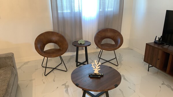 A modern living room with two leather armchairs, a small round table with a decorative coral, and a TV stand with a flat-screen TV and a router.
