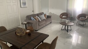 Una sala de estar moderna con comedor, que incluye un sofá, sillas, una mesa y suelo de mármol.