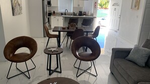 Una sala moderna con un sofá, dos sillones, una mesa de centro y un comedor con una mesa y sillas.