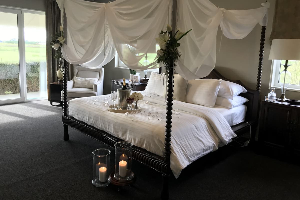 A four-poster canopy bed with a champagne bottle, glasses, and flowers on the bedside table.