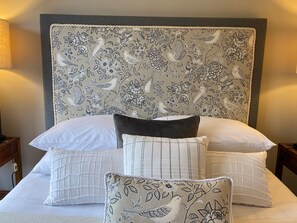 A bed with a floral-patterned headboard, white pillows, and a matching throw pillow.