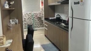 A modern kitchen with wooden cabinets, a white refrigerator, and a dining area with a table and chairs. - Charming apartment (PR)