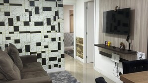 A modern living room with a sofa, a TV mounted on a wooden wall, a small table, and a patterned wall. - Charming apartment (PR)