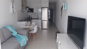 A modern kitchen with stainless steel appliances, a dining area with a white table and chairs, and a living area with a sofa and a flat-screen TV. - MARINE SENATOR (Costa Teguise)