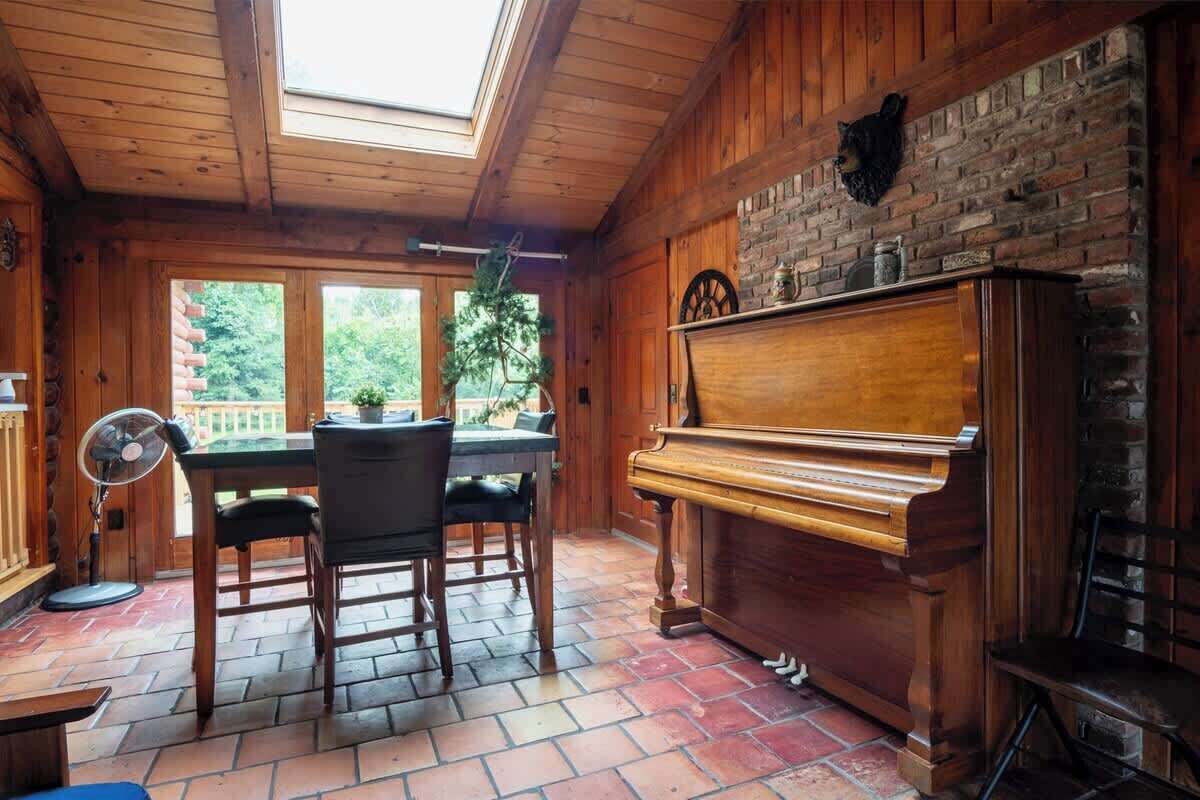 A wooden interior with a piano, dining table, chairs, and a fan.